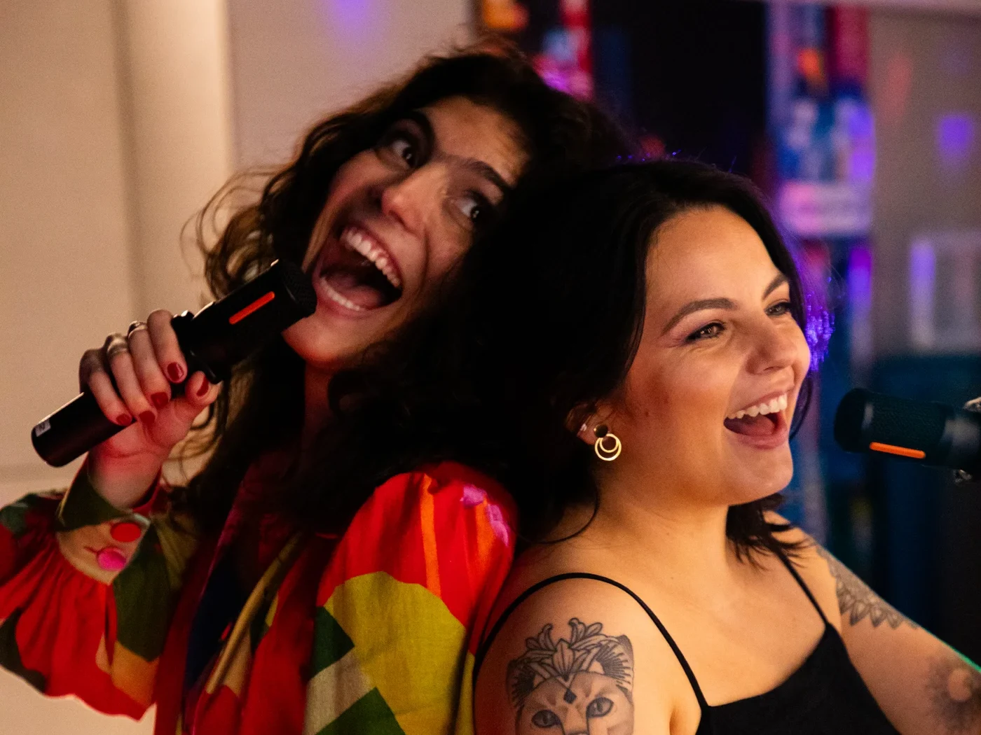 Amigas cantando e sorrindo em um camarote colorido