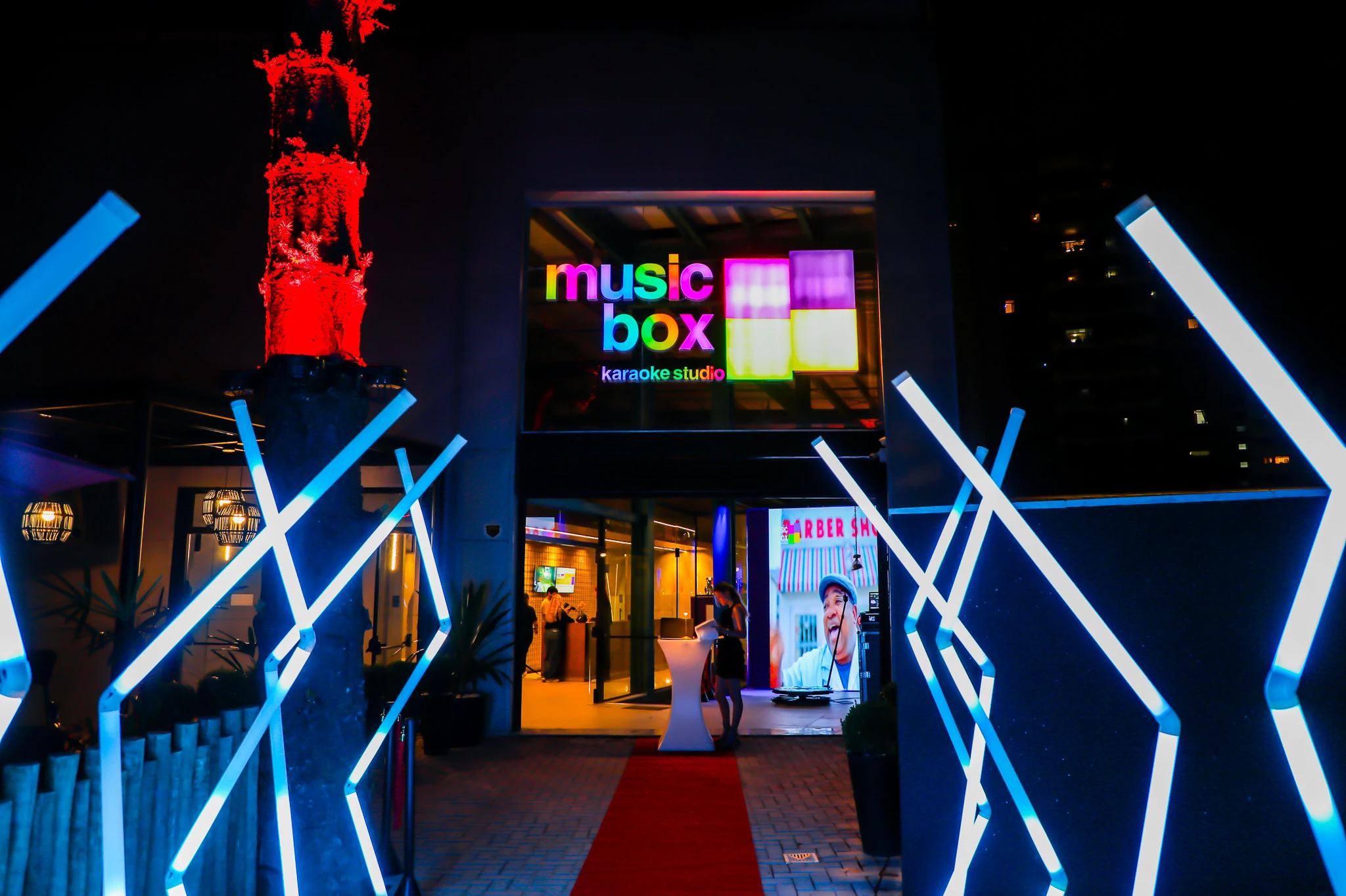 Fachada de entrada do Music Box Karaokê Studio iluminada à noite, com tapete vermelho